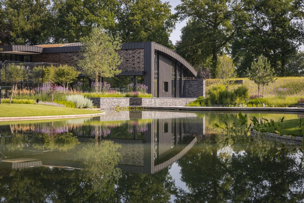 Een stijlvol modern huis met een vijver en bomen eromheen, die samen een harmonieus beeld geven.
